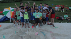 Group of kids and adults posing for a picture with sandcastle in front of them