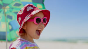 Little girl smiling wearing a summer hat and sunglasses